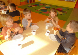 Czwórka dzieci je pizzę.